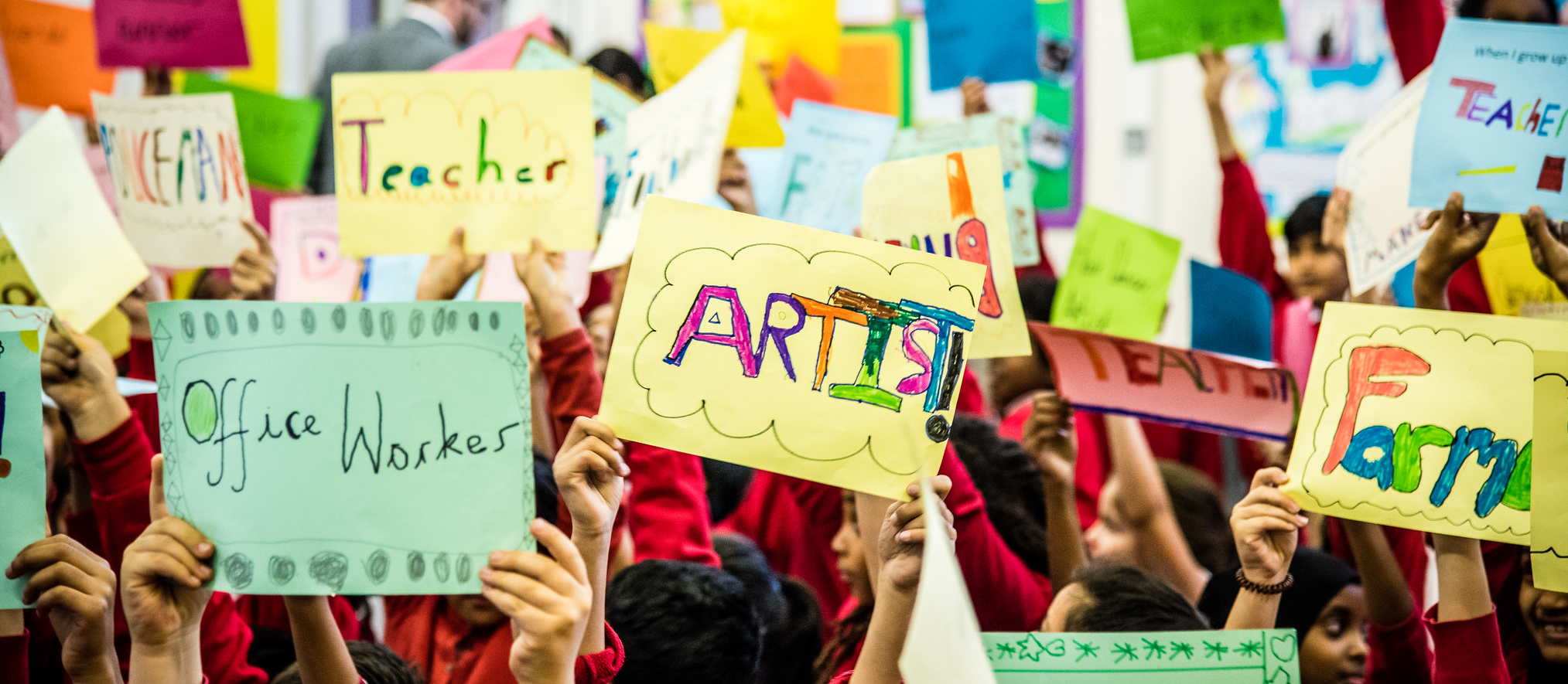 Children hold up colourful signs of the jobs they want when they grow up: artist, office worker, teacher