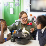 Uniformed pilot sat at desk talking with two pupils