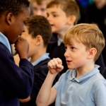 Two young boys from primary schools mock interviewing each other, talking into their pretend microphones as part of Inspiring the Future local media event in Bolton primary school